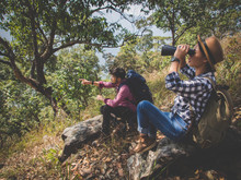 The Tourist Couple Sitting Use Binoculars On The Mountain.