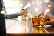 © ipopba - Close-up of two men clinking whiskey drink alcoholic beverage at bar counter in the pub background.