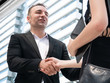 © natsarun - Confident business people shaking hands and smiling while standing at front modern office at the city center. Business partnership outdoor meeting. business colleagues teamwork, successful concept