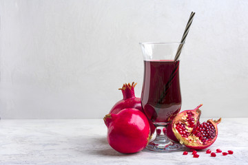 Red pomegranate juice in a glass, ripe and cut pomegranate and a sprig of mint on a gray concrete background. Vitamin, antioxidant and health food concept. Flat lay.Top view.