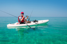 Man On A Fishing Kayak Shows Catch Fish. Leisure Activities On The Sea. Fisherman On The Islands.