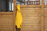 Fototapeta Tęcza - Yellow raincoat hanging in stable entrance