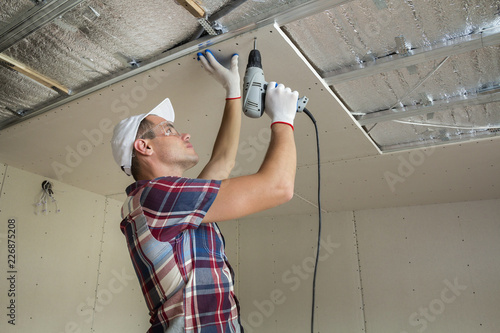 Young Man In Usual Clothing And Work Gloves Fixing Drywall