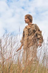 Wall Mural - young man dressed as a medieval peasant amidst wild yellowed ears against a blue sky