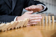© Freedomz - Wooden game strategy, Businessman hand stopping falling wooden dominoes effect from continuous toppled or risk and protection, strategy and successful intervention concept for business