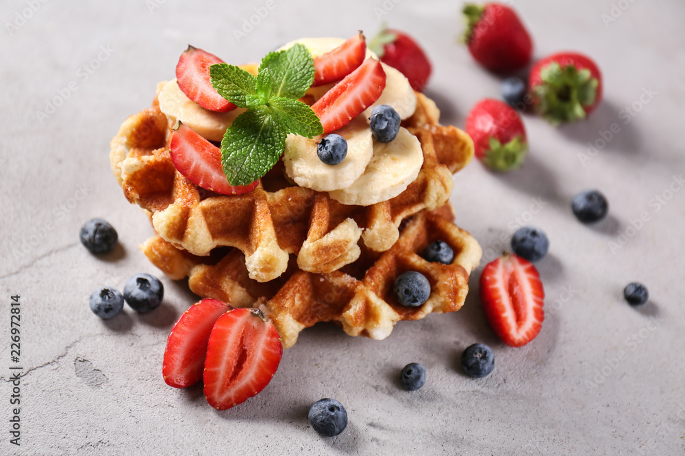 Delicious waffles with berries and banana on grey table