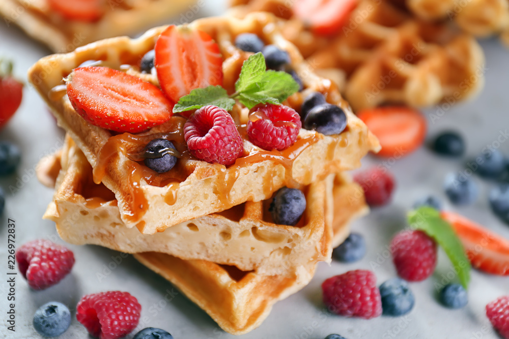 Delicious waffles with berries and caramel sauce on grey table