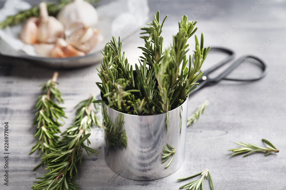 Metal cup with fresh rosemary on light table