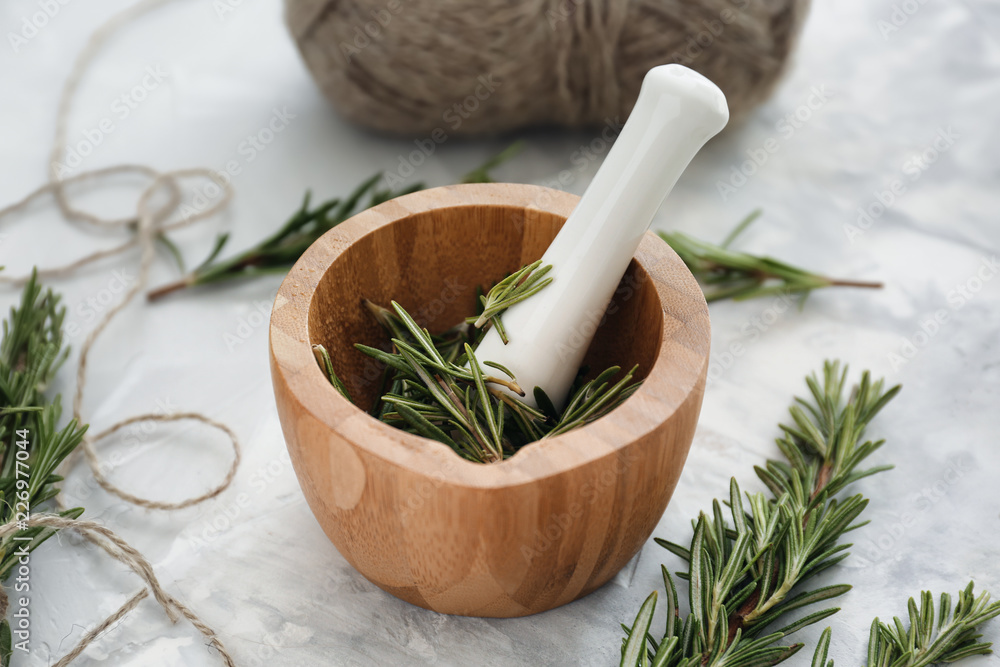 Mortar with fresh rosemary and pestle on light table