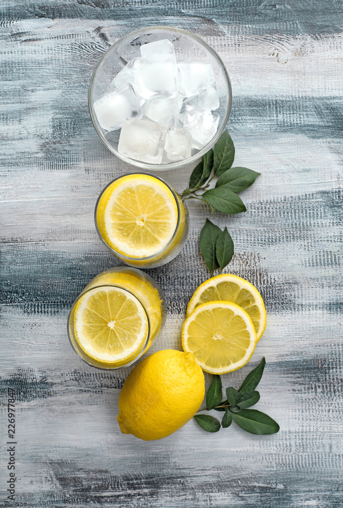 Glasses with lemon slices and ice cubes on wooden table