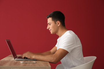 Sticker - Young man working with laptop while sitting at table against color background