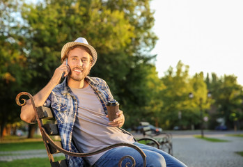 Sticker - Handsome young man with coffee talking by mobile phone in park