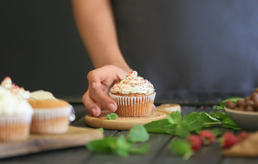 Woman taking delicious cupcake from wooden board, closeup