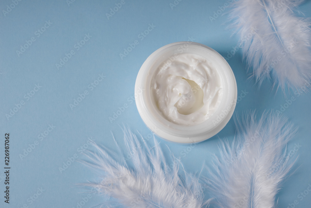 Jar with body cream and feathers on color background