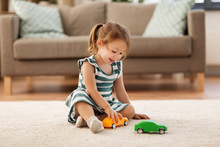Childhood And People Concept - Happy Three Years Old Baby Girl Playing With Toy Car At Home