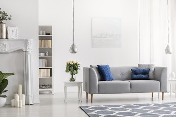 Wall Mural - Grey settee with blue cushions in white elegant living room interior with flowers and painting. Real photo