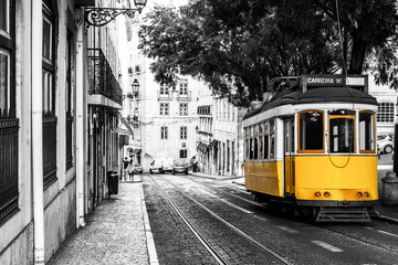 Yellow tram on old streets of Lisbon, Portugal, popular touristic attraction and destination. Black and white picture with a coloured tram.