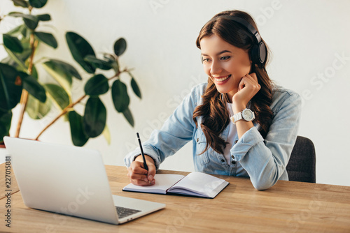 Fotografía portrait of young smiling woman in headphones taking part in webinar in office