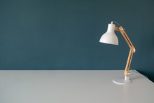 Office Work Desk With Office Lamp In A Dark Blue Green Background. White Desk With Copy Space