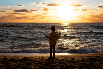 Little girl standing on the beach at the sunset time.