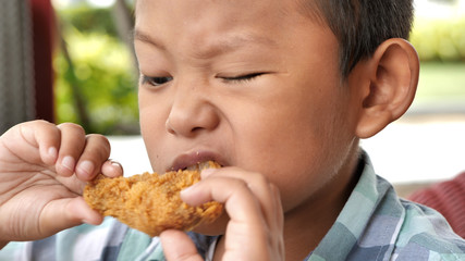 Cute asian boy are happy eating fried chicken leg in restaurant