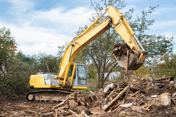 Excavator bucket loading construction debris after demolishing house