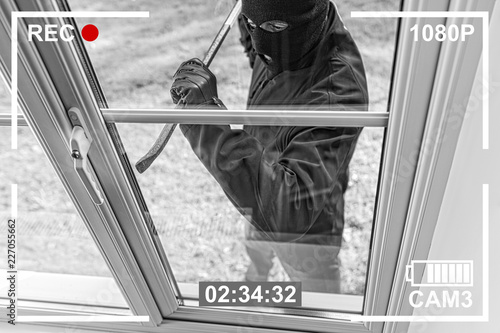 Fotomural CCTV view of burglar breaking in to home through window