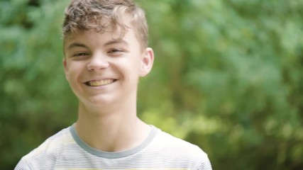 Wall Mural - Close up emotional portrait of caucasian smiling teen boy. Handsome guy. Funny cute teenager in summer park at day. Child looking at camera.