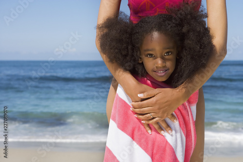 Fotografie, Obraz Mother and daughter on sandy beach wrapped in striped towel at camera