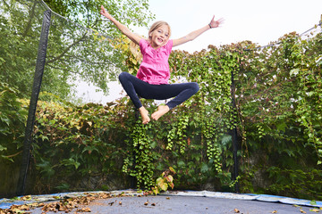 Child girl jumping on trampoline with greenery background