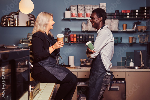 Foto Two young multiracial baristas relaxing after work laughing and talking together at the trendy coffee shop