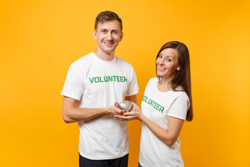 Portrait of young colleagues couple in white t-shirt with written inscription green title volunteer isolated on yellow background. Voluntary free work, assistance help, charity grace teamwork concept.