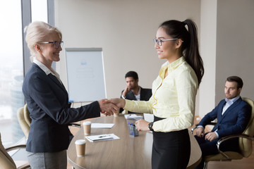 Sticker - Smiling middle aged businesswoman handshake Asian employee congratulating with promotion, happy female boss shake hand of millennial woman worker greeting with good work results. Reward concept