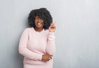 Poster - Young african american plus size woman over grey grunge wall wearing winter sweater pointing finger up with successful idea. Exited and happy. Number one.