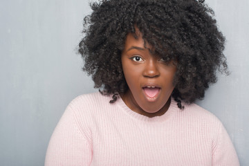 Canvas Print - Young african american plus size woman over grey grunge wall wearing winter sweater afraid and shocked with surprise expression, fear and excited face.