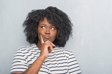 Canvas Print - Young african american plus size woman over grey grunge wall with hand on chin thinking about question, pensive expression. Smiling with thoughtful face. Doubt concept.