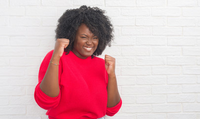 Poster - Young african american plus size woman over white brick wall very happy and excited doing winner gesture with arms raised, smiling and screaming for success. Celebration concept.