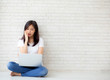 © NT_studio - Beautiful of portrait asian young woman working online laptop and thinking and serious sitting on floor brick cement background, freelance girl using notebook computer, business and lifestyle concept.