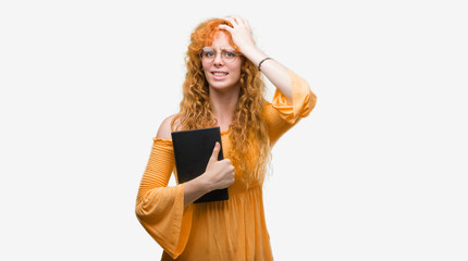 Poster - Young redhead student woman holding a book stressed with hand on head, shocked with shame and surprise face, angry and frustrated. Fear and upset for mistake.