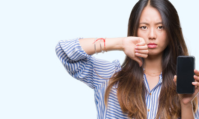 Sticker - Young asian woman showing blank screen of smartphone over isolated background with angry face, negative sign showing dislike with thumbs down, rejection concept