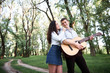 © soleg - young couple walking in the forest and playing guitar, summer nature, bright sunlight, shadows and green leaves, romantic feelings