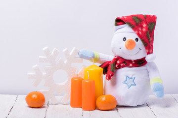 Funny snowman with mandarins and candles on a white wooden background