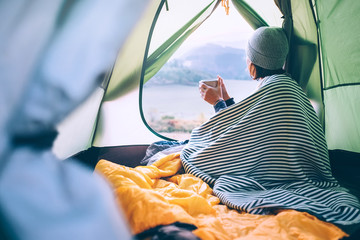 Woman drinks hot tea in camping tent and enjoy with autumn evening in mountain valley