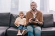 © LIGHTFIELD STUDIOS - father and little little son sitting on couch and playing with joysticks