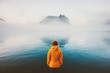 Woman alone looking at foggy sea traveling adventure lifestyle outdoor solitude sad emotions winter down jacket clothing cold scandinavian minimal landscape