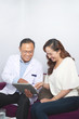 © DragonImages - Smiling doctor explaining to his patient details of operation and showing it on touchpad while they sitting on sofa at office