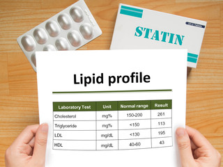 Physician checking blood laboratory results of lipid profile in high cholesterol patient and generic pack of statins tablets for treatment dyslipidemia on wood table. Health care and medical concept.