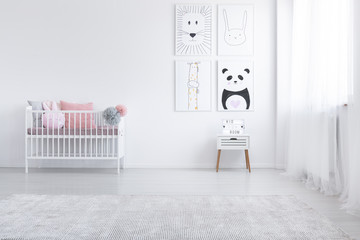 Pink pillow in cradle and posters on the wall in white child's room interior with carpet. Real photo