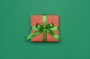 Wall Mural - Gift box with green ribbon on green background top view flat lay. Holiday concept, birthday gift, new year or Christmas gift box presents Xmas holiday. Congratulations background with space for text.