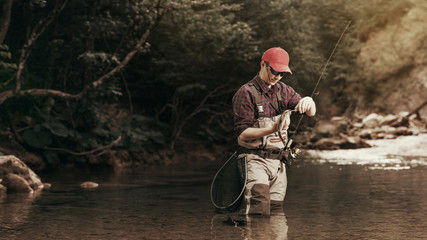 Fisherman caught a fish takes the hook. Trout fishing on the river.